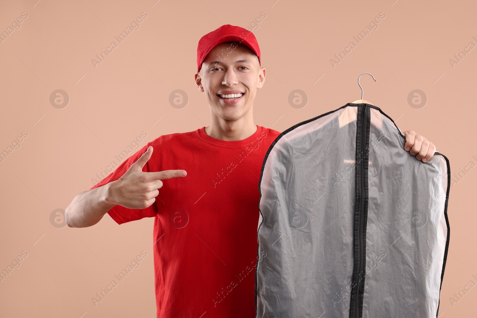 Photo of Dry-cleaning delivery. Happy courier holding garment cover with clothes on beige background