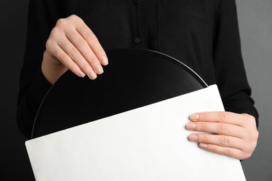Photo of Woman taking vinyl record out of paper sleeve on grey background, closeup