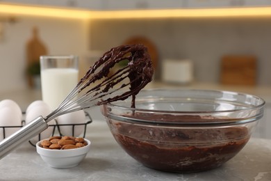 Photo of Whisk with chocolate cream, bowl and different products on gray marble table in kitchen