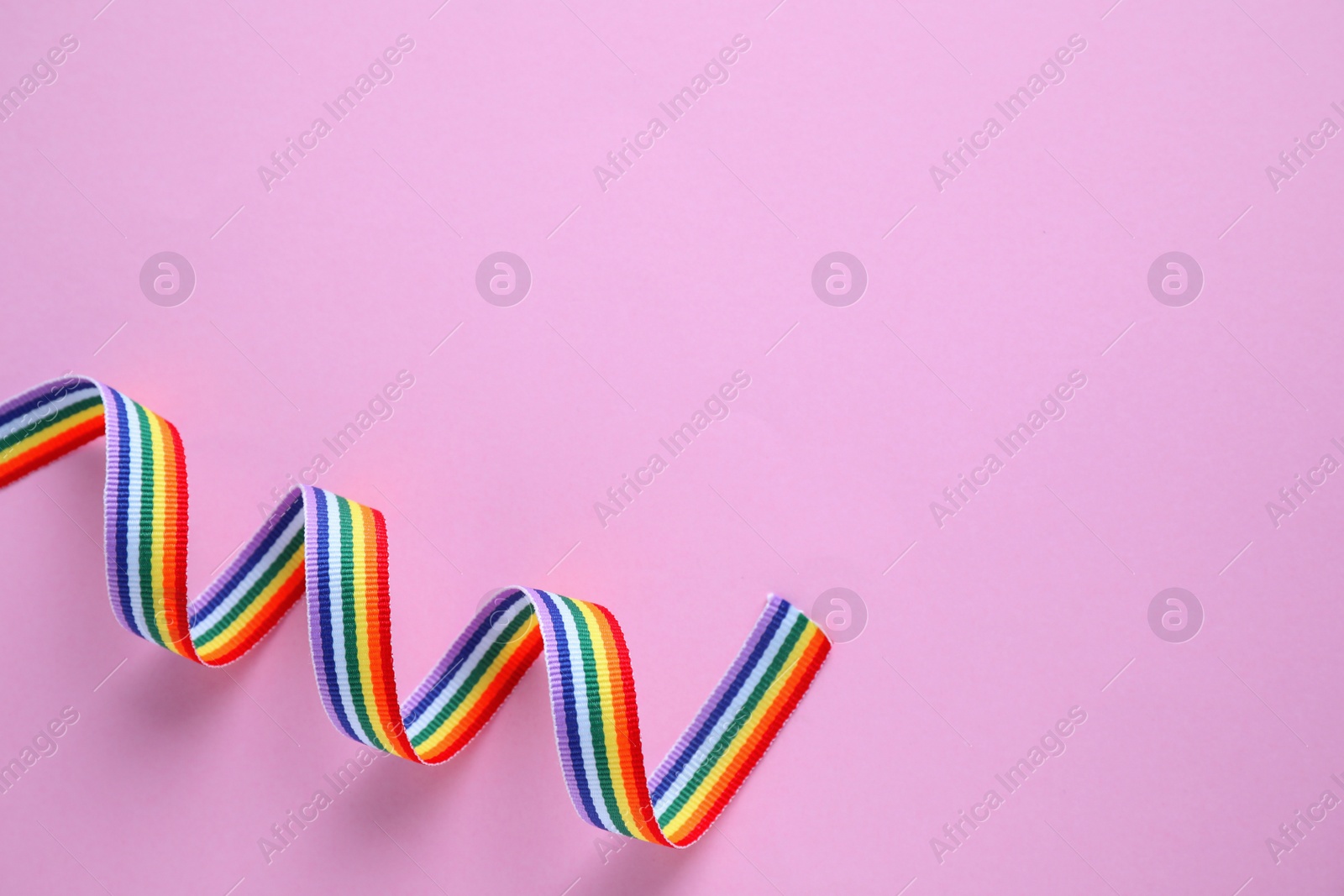 Photo of Bright rainbow ribbon on color background, top view with space for text. Symbol of gay community