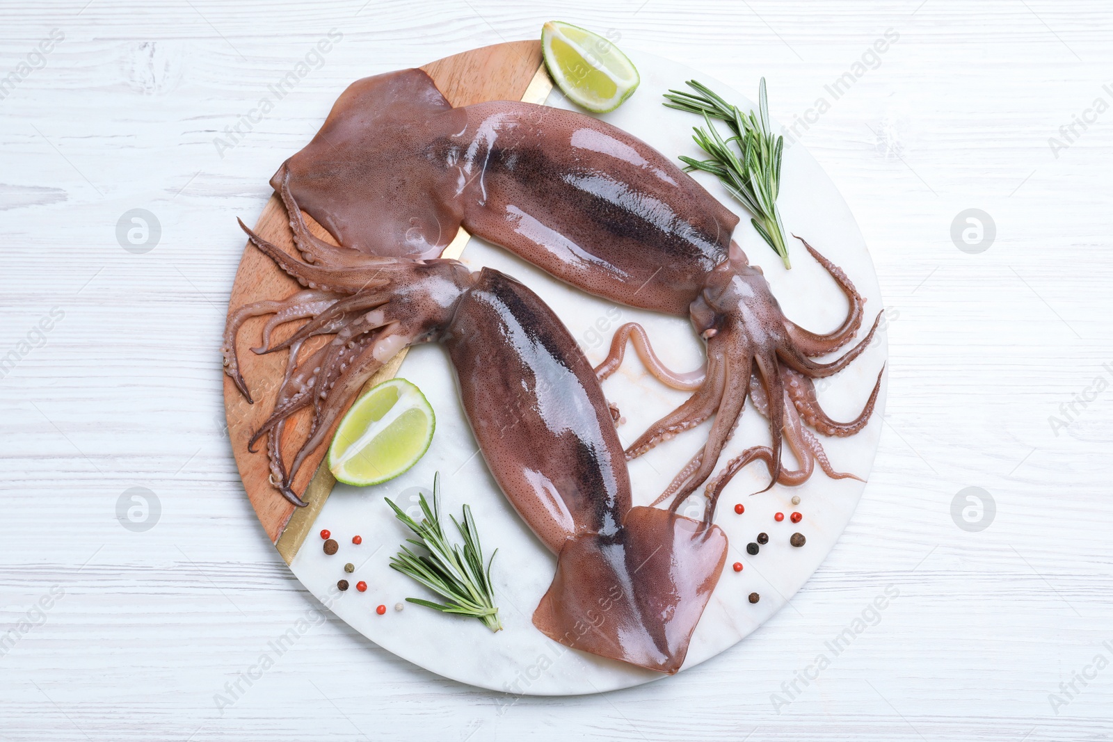 Photo of Fresh raw squids with lime and rosemary on white wooden table, top view