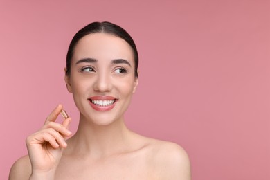 Photo of Beautiful young woman with vitamin pill on pink background. Space for text