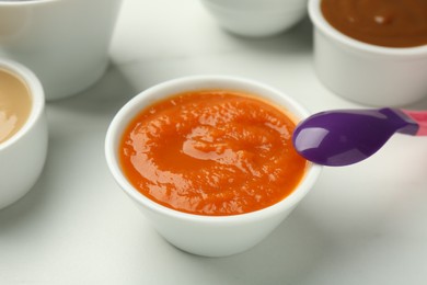 Bowl with healthy baby food and spoon on white table, closeup