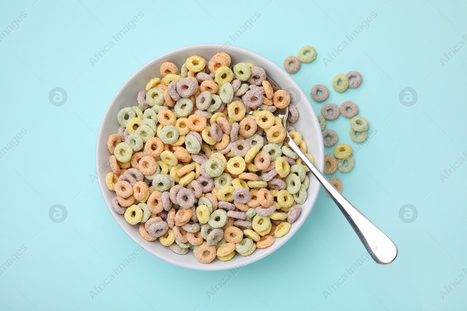 Photo of Tasty cereal rings in bowl and spoon on light blue table, top view