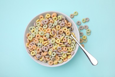 Photo of Tasty cereal rings in bowl and spoon on light blue table, top view