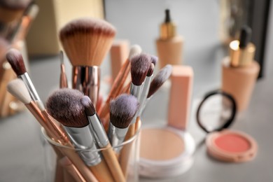 Photo of Set of professional brushes and makeup products near mirror on grey table, closeup. Space for text