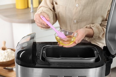 Photo of Woman spreading breadmaker pan with oil, closeup