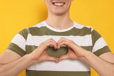 Photo of Happy volunteer making heart with his hands on orange background, closeup