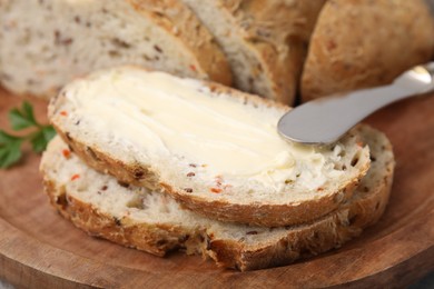 Tasty bread with butter and knife on wooden board, closeup