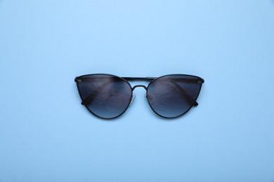 Stylish sunglasses on light blue background, top view