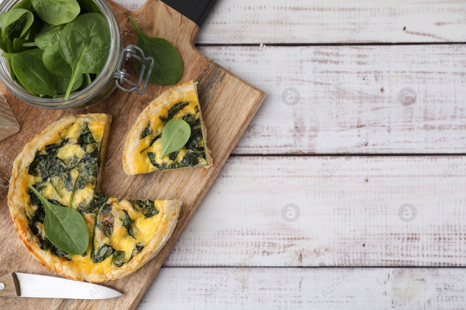 Photo of Delicious cut pie with spinach on white wooden table, top view. Space for text