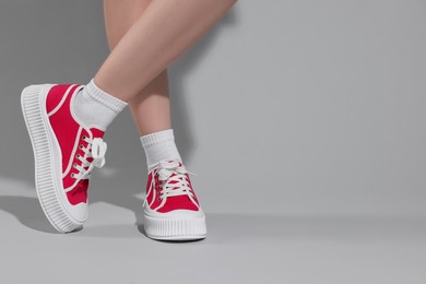 Woman wearing red classic old school sneakers on light gray background, closeup. Space for text