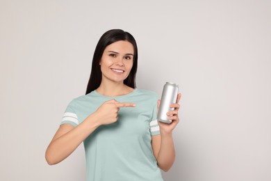 Photo of Beautiful young woman holding tin can with beverage on light grey background