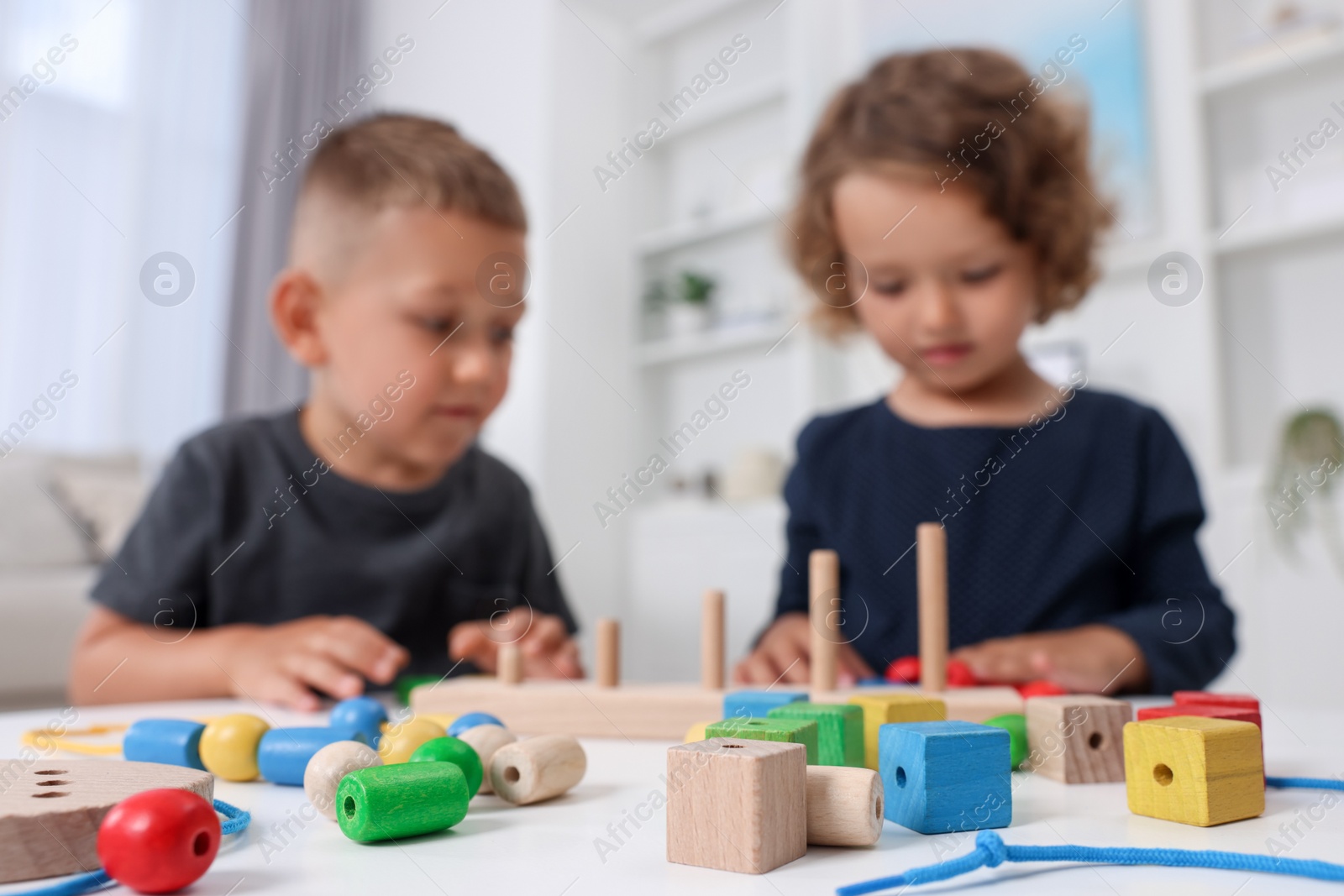 Photo of Motor skills development. Little kids playing with stacking and counting game at table indoors, selective focus. Space for text