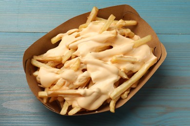 Photo of Tasty potato fries and cheese sauce in paper container on light blue wooden table, top view