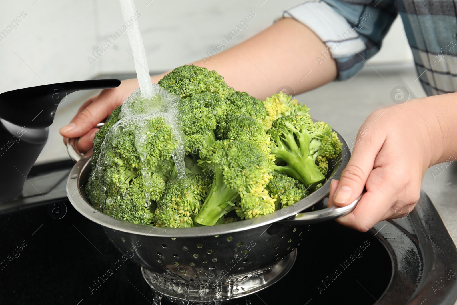 Photo of Woman washing fresh green broccoli in kitchen sink, closeup