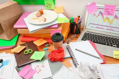 Photo of Messy table with laptop and stationery. Concept of being overwhelmed by work