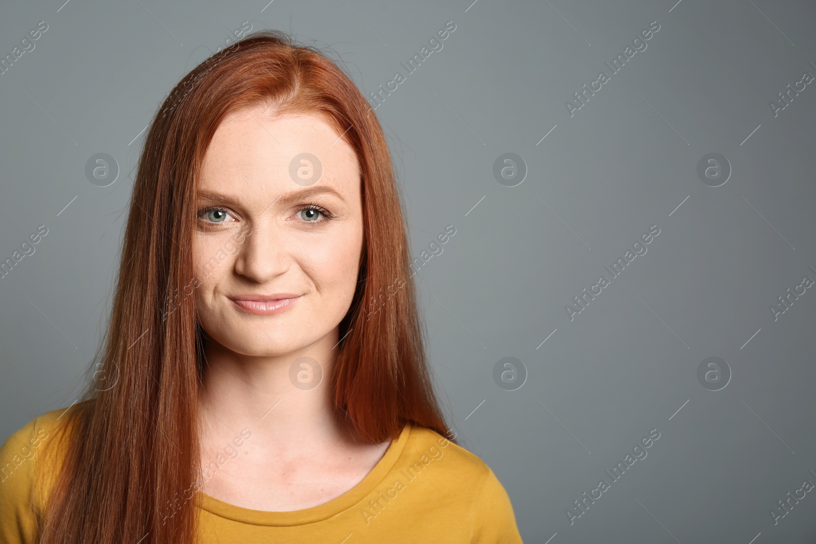 Photo of Candid portrait of happy young woman with charming smile and gorgeous red hair on grey background, space for text