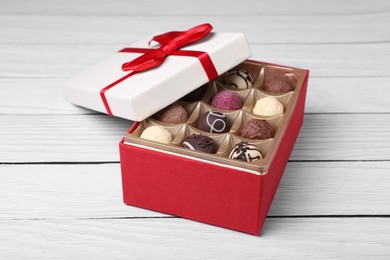 Photo of Red box with tasty chocolate candies on white wooden table