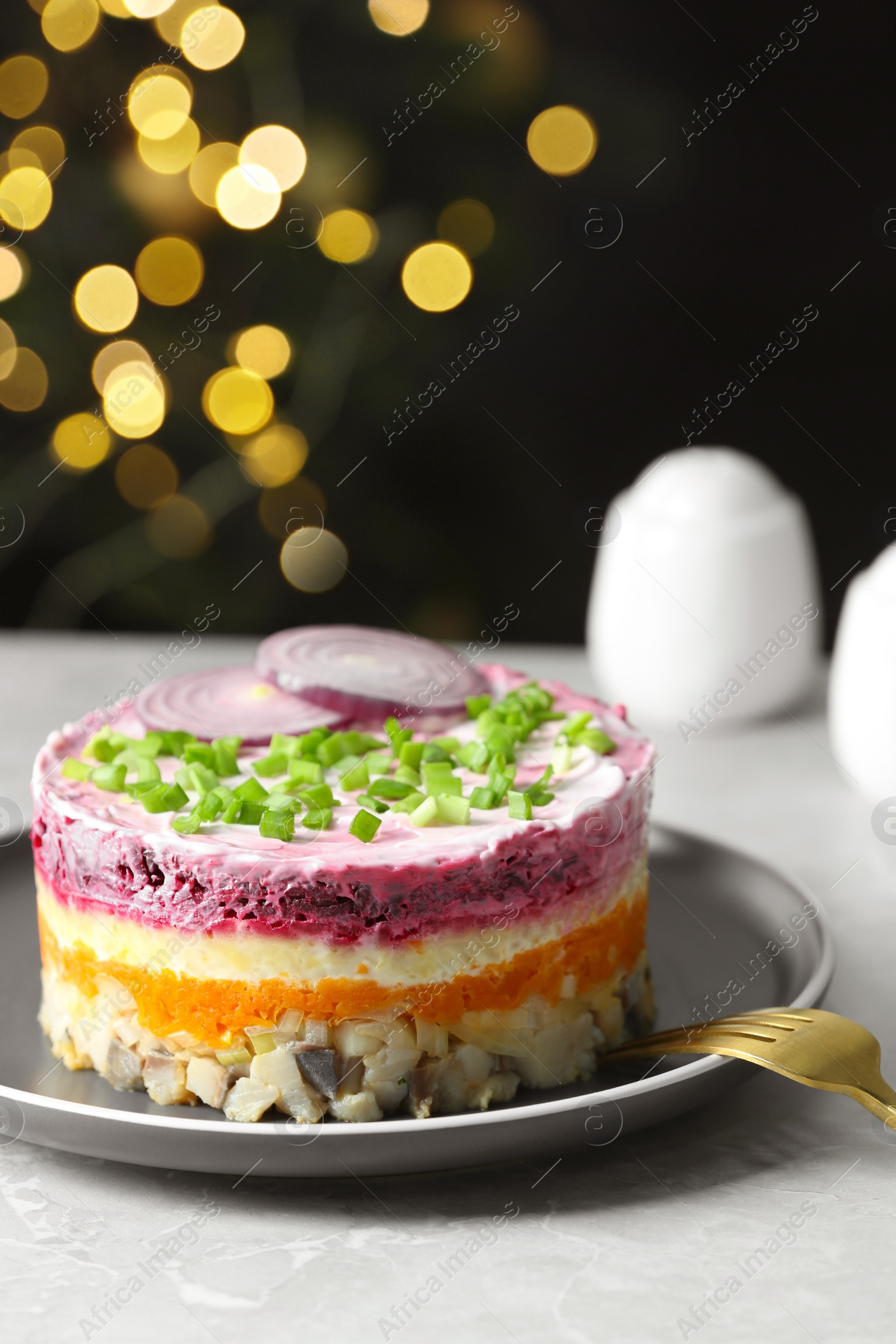 Photo of Herring under fur coat salad served on light grey table against blurred festive lights, space for text. Traditional Russian dish