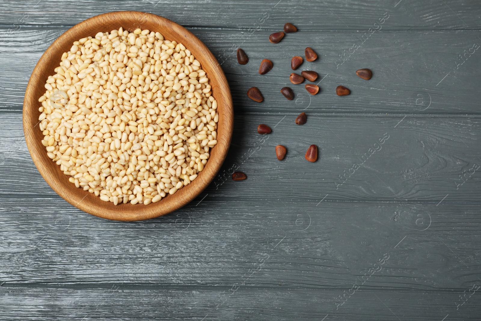 Photo of Dish with pine nuts on wooden background, top view. Space for text