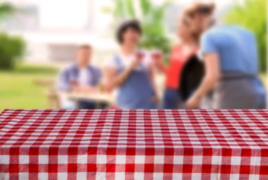 Image of Table with checkered picnic cloth outdoors on sunny day. Space for design