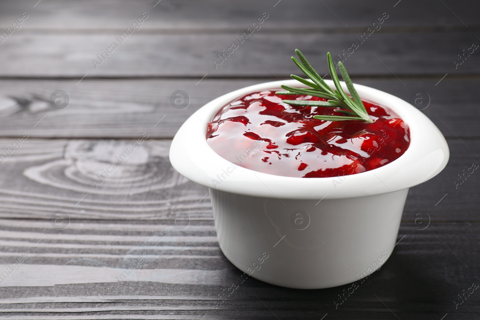 Photo of Fresh cranberry sauce in bowl and rosemary on black wooden table, closeup. Space for text