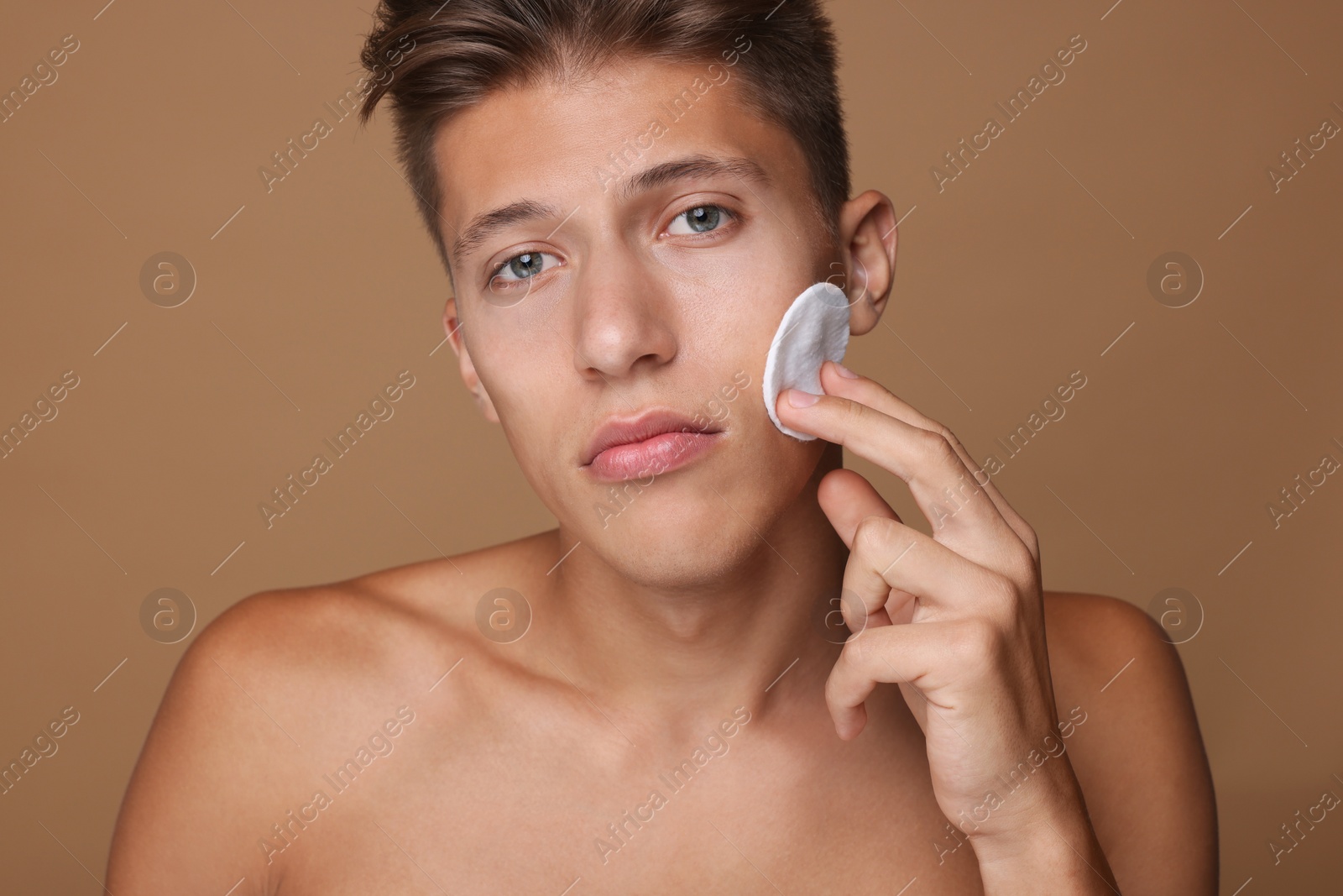 Photo of Handsome man cleaning face with cotton pad on beige background