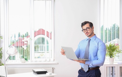 Handsome young man with laptop at workplace, space for text