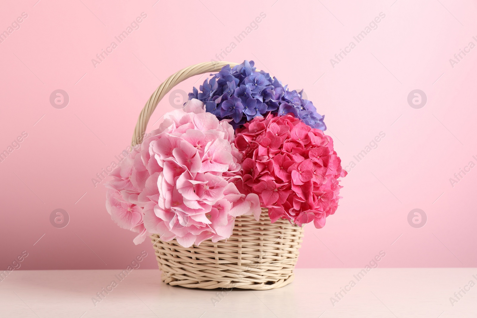 Photo of Bouquet with beautiful hortensia flowers in wicker basket on white wooden table