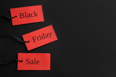 Red tags with words BLACK FRIDAY SALE on dark background, flat lay. Space for text