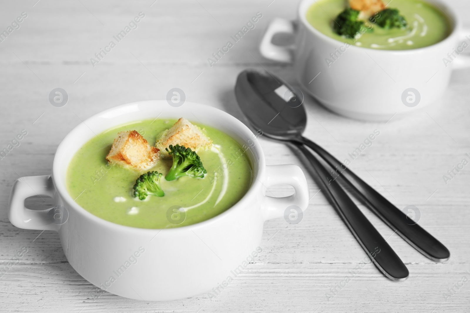 Photo of Delicious broccoli cream soup with croutons served on white wooden table