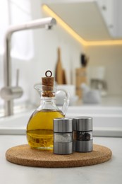Photo of Salt and pepper mills with bottle of oil on table in kitchen