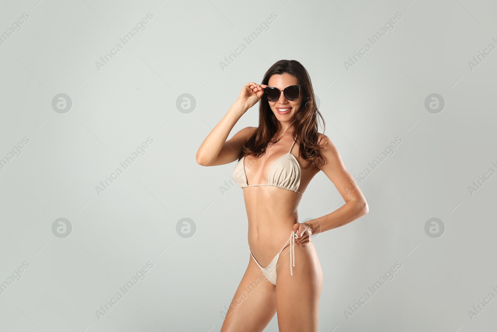 Photo of Beautiful woman in stylish bikini and sunglasses on light grey background. Space for text