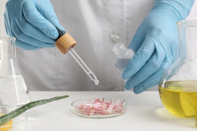 Scientist developing cosmetic oil at white table, closeup