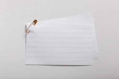 Sheets of paper attached with safety pin on white background, top view