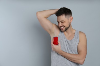Photo of Handsome man applying deodorant on grey background. Space for text