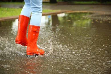 Photo of Woman with red rubber boots jumping in puddle, closeup. Rainy weather