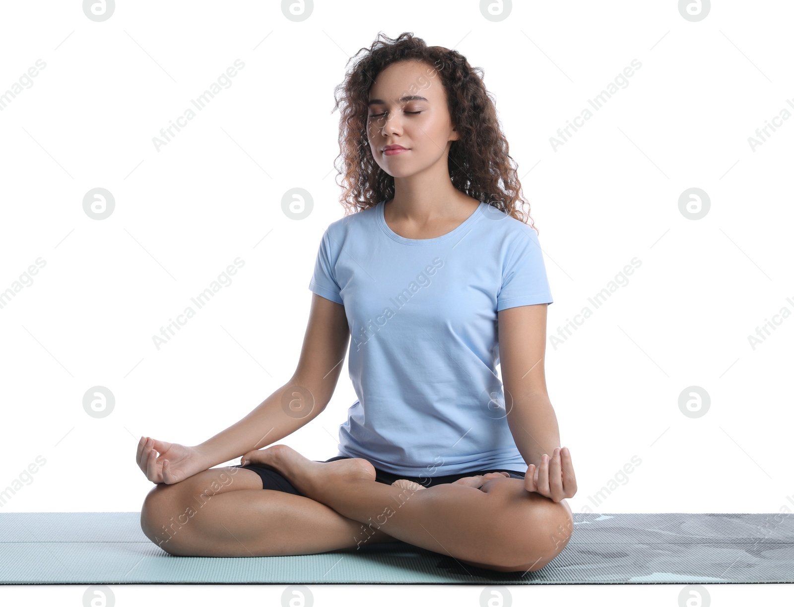 Photo of Beautiful African-American woman meditating on yoga mat against white background