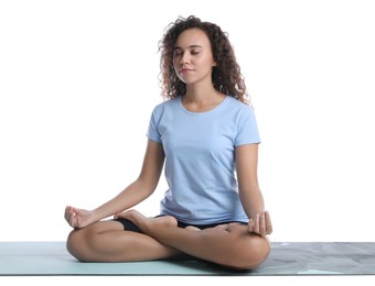 Beautiful African-American woman meditating on yoga mat against white background