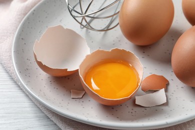 Whole and cracked chicken eggs on white wooden table, closeup