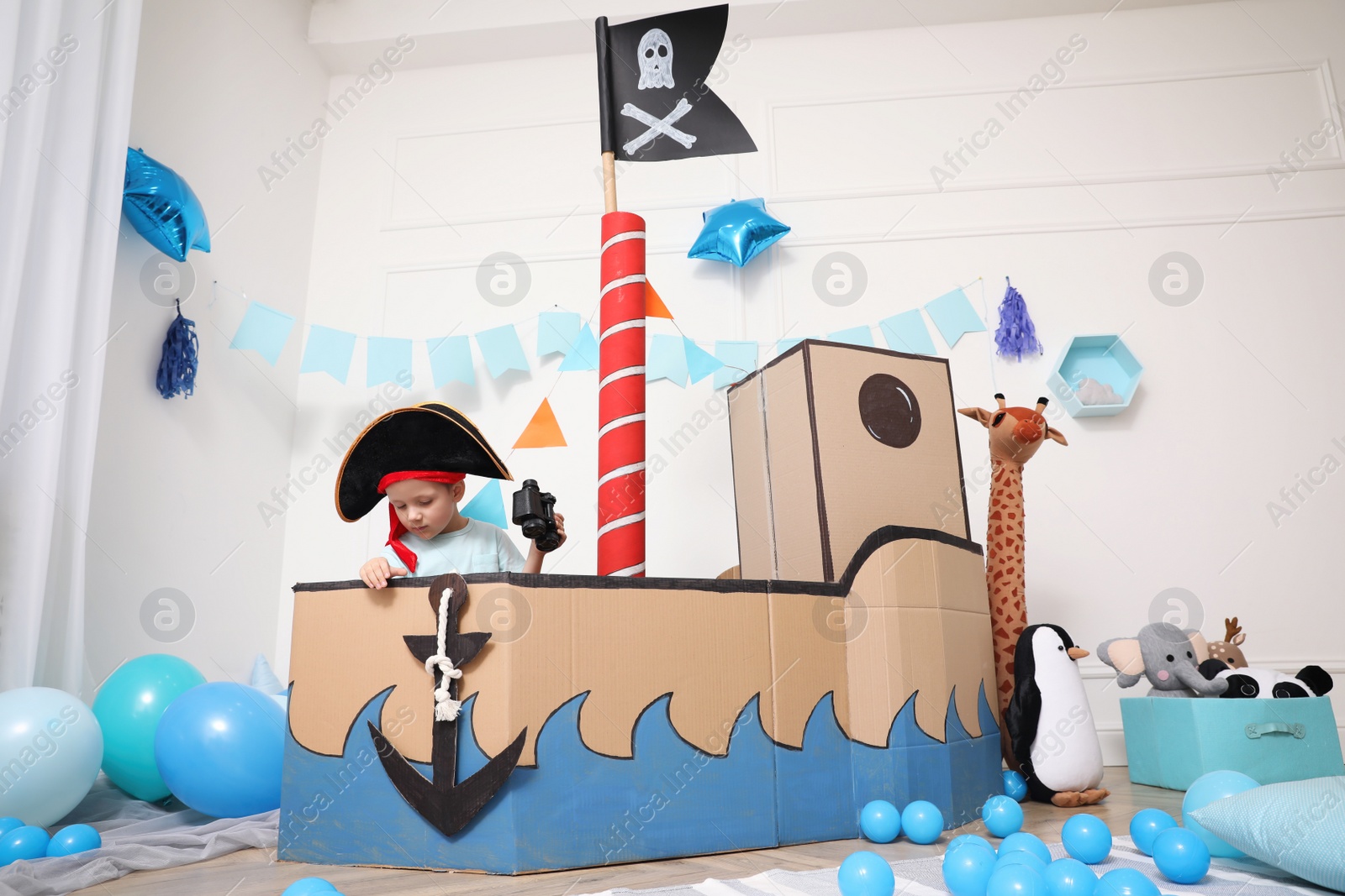 Photo of Little boy playing with binoculars in pirate cardboard ship at home. Child's room interior