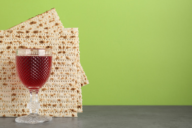 Photo of Passover matzos and glass of wine on grey table, space for text. Pesach celebration