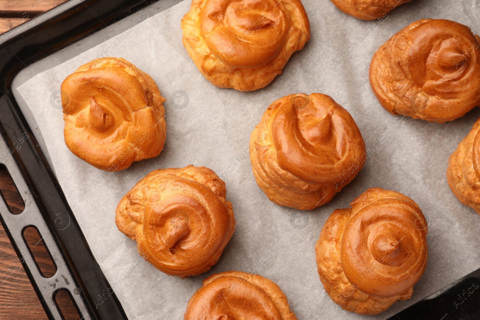 Photo of Delicious profiteroles on baking pan, top view