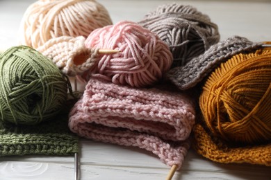 Balls of soft yarns, knitting and needles on white wooden table