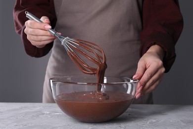 Photo of Woman with whisk mixing chocolate cream at table against grey background, closeup