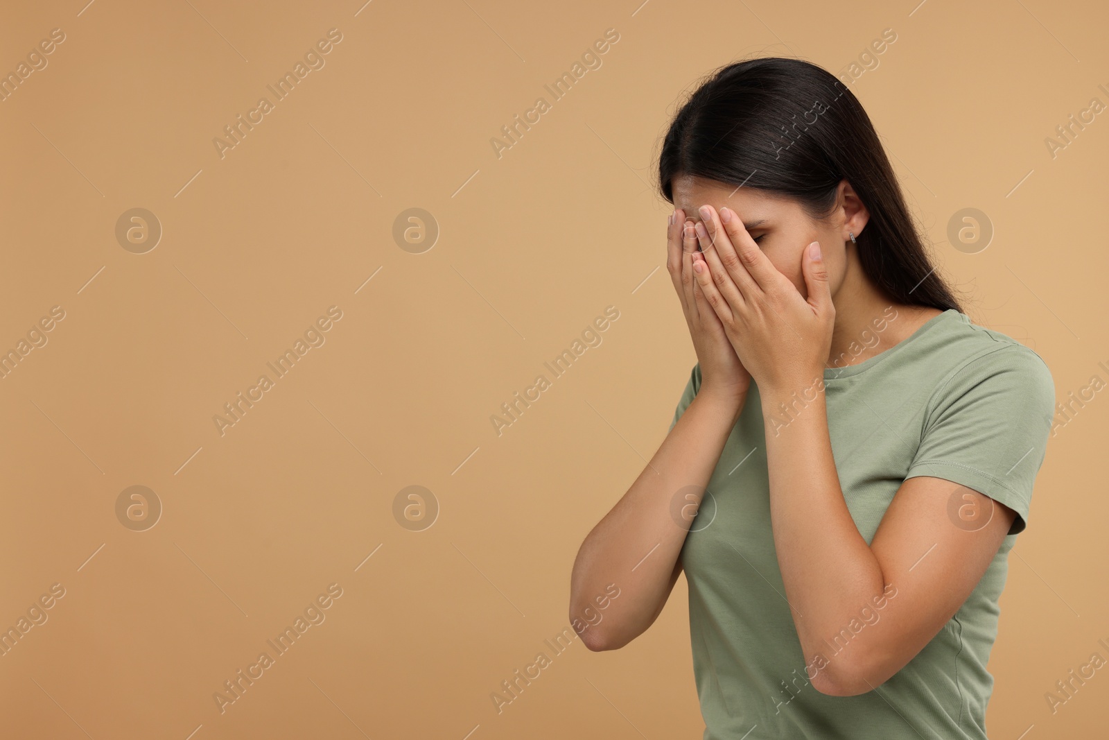 Photo of Resentful woman covering face with hands on beige background, space for text