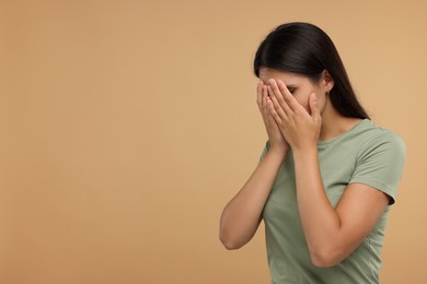 Resentful woman covering face with hands on beige background, space for text