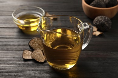 Photo of Fresh truffle oil in glass jug on black wooden table