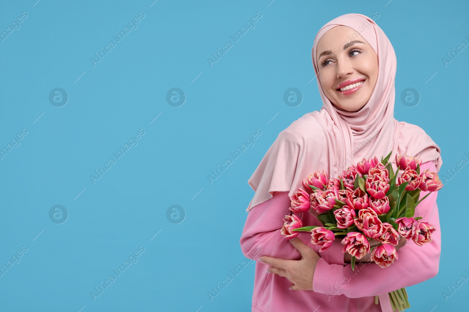 Photo of Happy woman in hijab with beautiful bouquet on light blue background. Space for text